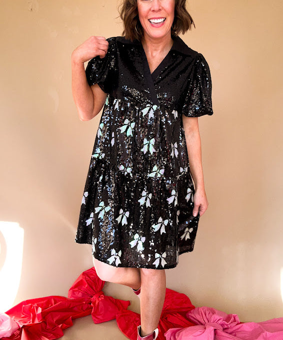 Black sequined mini dress with a silk V-neckline and balloon sleeves, an empire waist with white sequined bows on the skirt. 