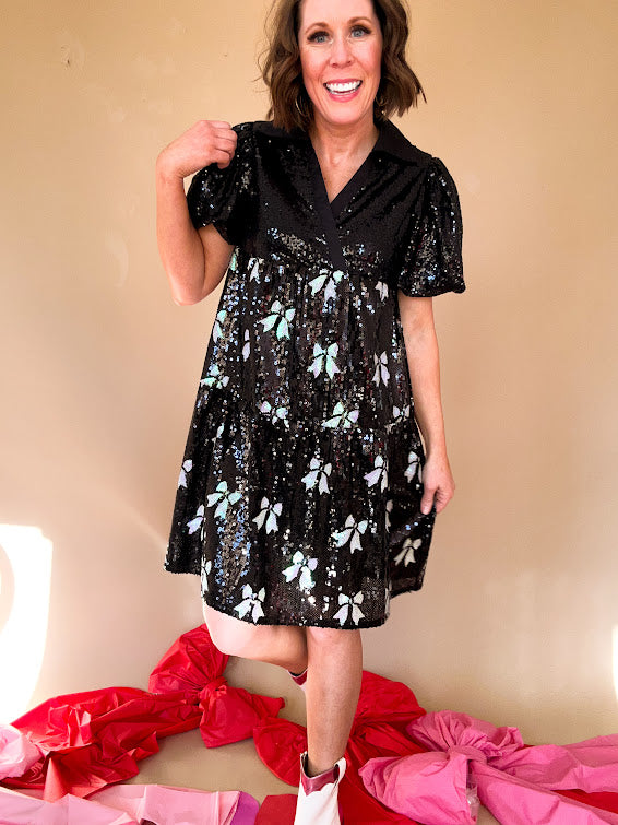 Black sequined mini dress with a silk V-neckline and balloon sleeves, an empire waist with white sequined bows on the skirt. 