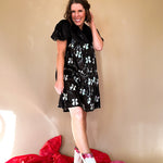 Black sequined mini dress with a silk V-neckline and balloon sleeves, an empire waist with white sequined bows on the skirt. 