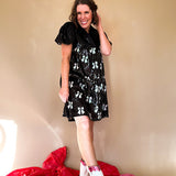 Black sequined mini dress with a silk V-neckline and balloon sleeves, an empire waist with white sequined bows on the skirt. 