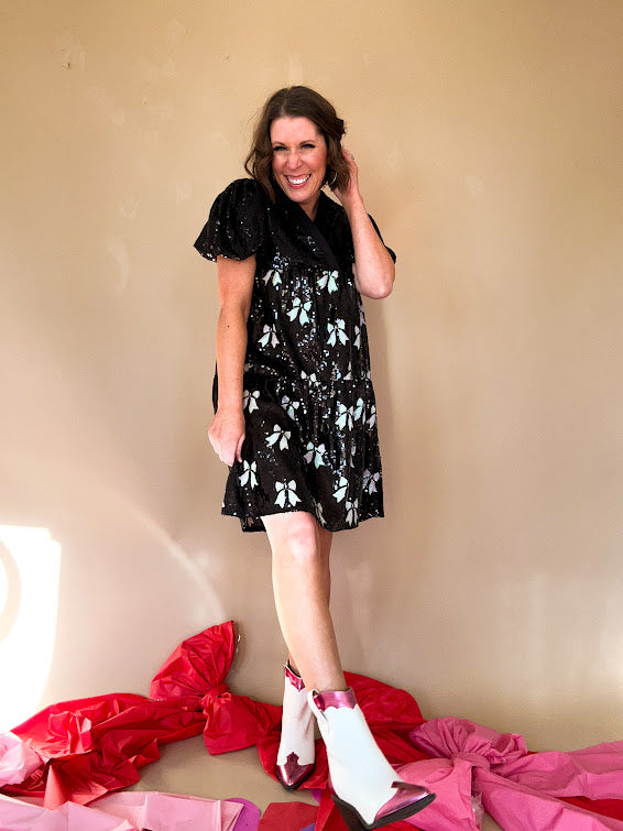 Black sequined mini dress with a silk V-neckline and balloon sleeves, an empire waist with white sequined bows on the skirt. 