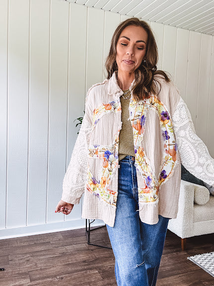 Beige cotton shacket with floral peace patch across the front, lace sleeves and metal buttons down the front. Oversized.