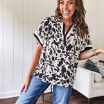 Thin, lightweight black and cream tropical print drop shoulder blouse with cream and black striping at the V neck, and short sleeve cuffs, standard collar and split flowy hem.