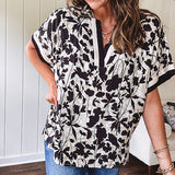 Thin, lightweight black and cream tropical print drop shoulder blouse with cream and black striping at the V neck, and short sleeve cuffs, standard collar and split flowy hem.
