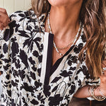 Thin, lightweight black and cream tropical print drop shoulder blouse with cream and black striping at the V neck, and short sleeve cuffs, standard collar and split flowy hem.
