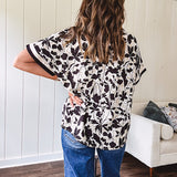 Thin, lightweight black and cream tropical print drop shoulder blouse with cream and black striping at the V neck, and short sleeve cuffs, standard collar and split flowy hem.