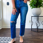 High rise dark wash denim with button and zipper closure, stretch, distressing at the knee and raw hem with straight leg.