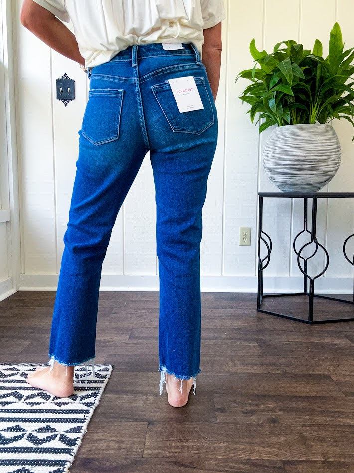 High rise dark wash denim with button and zipper closure, stretch, distressing at the knee and raw hem with straight leg.