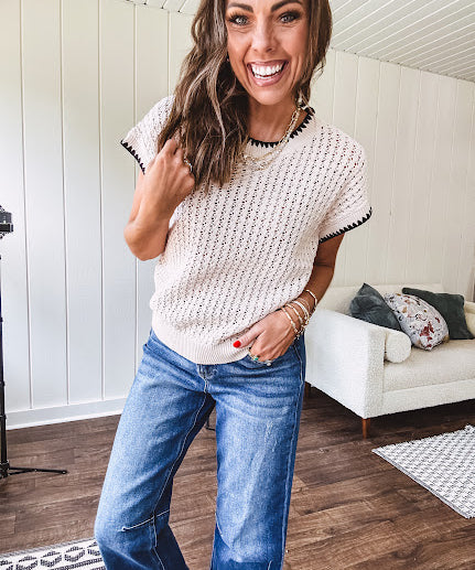 Light khaki crochet knit sweater with short sleeves and contrasting black trim at the round neck and cuffs with a wide ribbed hem.