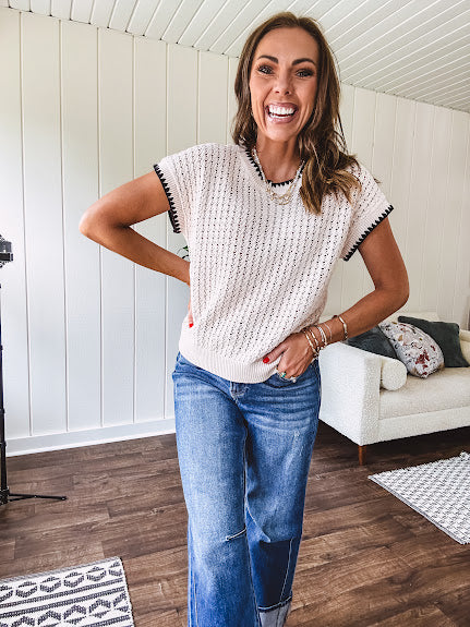 Light khaki crochet knit sweater with short sleeves and contrasting black trim at the round neck and cuffs with a wide ribbed hem.