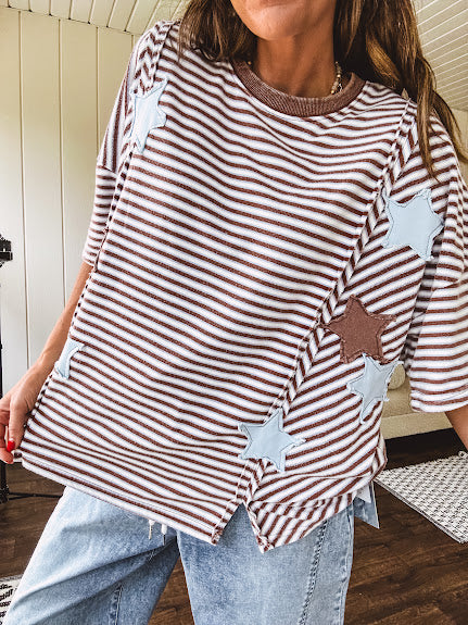 Oversized terry knit short sleeved top with cream, espresso and light blue striping and star patches throughout with exposed seams down the sides of the front and a split front hem.