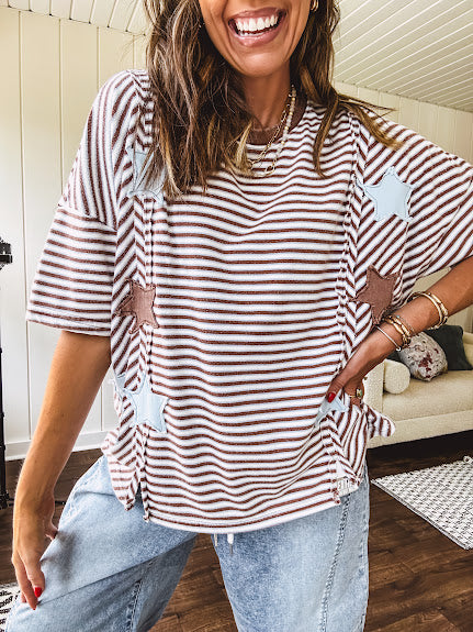 Oversized terry knit short sleeved top with cream, espresso and light blue striping and star patches throughout with exposed seams down the sides of the front and a split front hem.