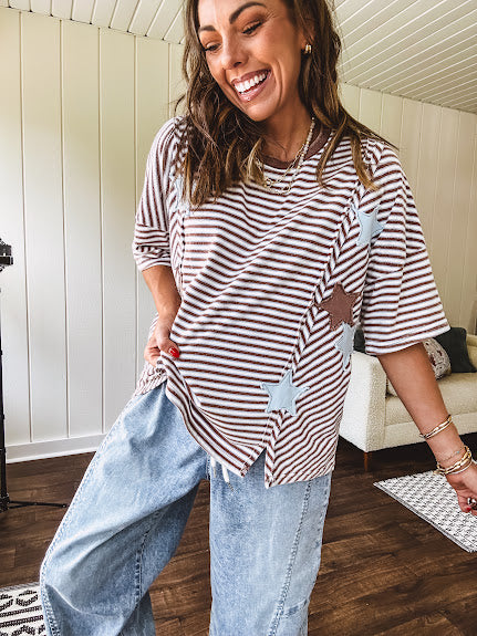 Oversized terry knit short sleeved top with cream, espresso and light blue striping and star patches throughout with exposed seams down the sides of the front and a split front hem.