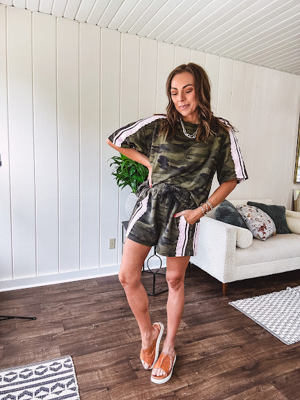 Thin, lightweight dark camo shorts with elastic drawstring waist, side pockets and light pink striping and lace detail down the sides.