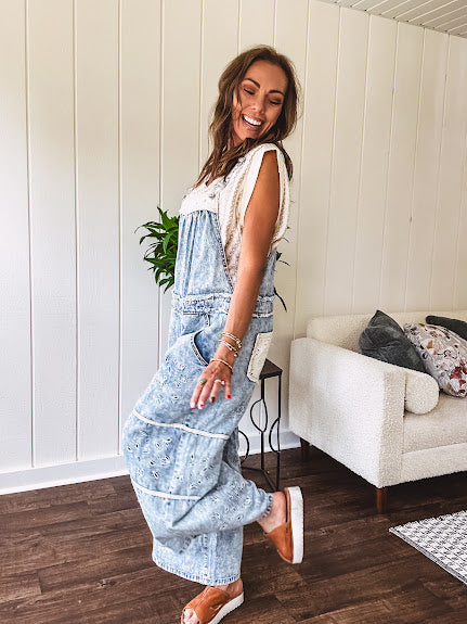 Vintage light wash denim and twill overalls with silver metal adjustable strap hardware, side zip, side and back pockets with ivory eyelet trim and cutouts throughout, wide leg design.