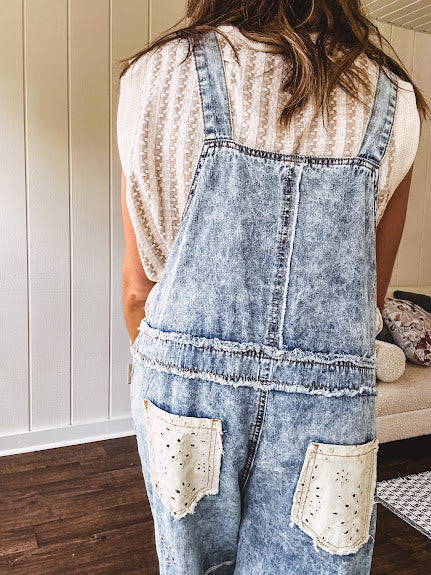 Vintage light wash denim and twill overalls with silver metal adjustable strap hardware, side zip, side and back pockets with ivory eyelet trim and cutouts throughout, wide leg design.