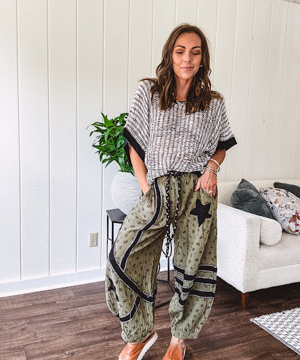 Cotton lightweight moss green joggers with mauve dainty floral print and black knit striping and star patch detail throughout, button and zipper closure with rope grommet stye belt, side pockets and elastic cuffs.