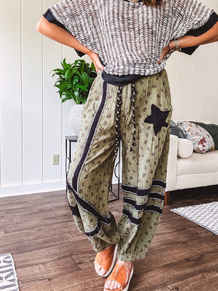 Cotton lightweight moss green joggers with mauve dainty floral print and black knit striping and star patch detail throughout, button and zipper closure with rope grommet stye belt, side pockets and elastic cuffs.