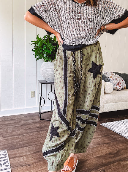 Cotton lightweight moss green joggers with mauve dainty floral print and black knit striping and star patch detail throughout, button and zipper closure with rope grommet stye belt, side pockets and elastic cuffs.