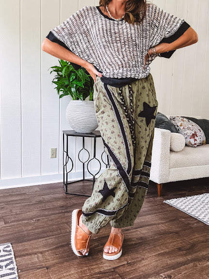 Cotton lightweight moss green joggers with mauve dainty floral print and black knit striping and star patch detail throughout, button and zipper closure with rope grommet stye belt, side pockets and elastic cuffs.