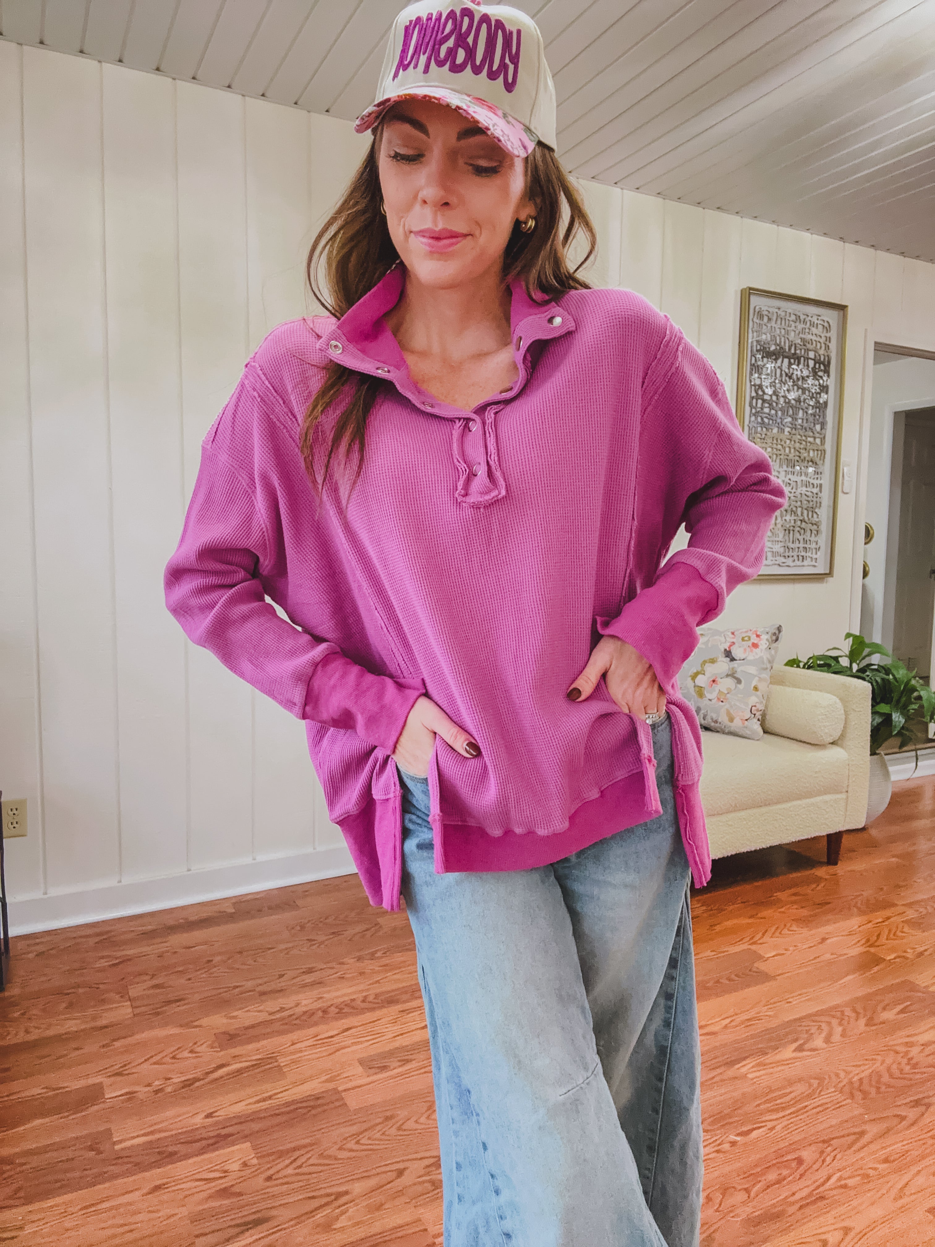 Woman wearing a pink sweatshirt and cap in a living room.