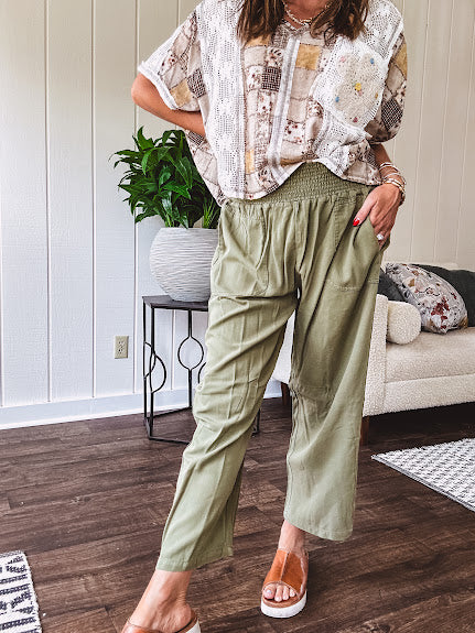 Lightweight olive smocked waist pants with side pockets and knee darts, cropped style.