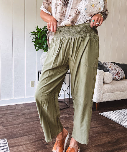 Lightweight olive smocked waist pants with side pockets and knee darts, cropped style.