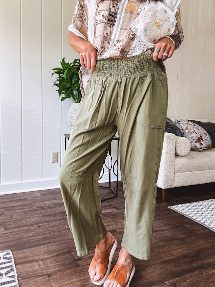 Lightweight olive smocked waist pants with side pockets and knee darts, cropped style.