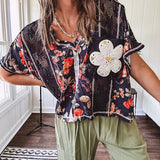 Lightweight black V neck tee with coral rose floral print throughout, raw seams and black ace inserts and ivory floral crochet patchwork on the front pocket.