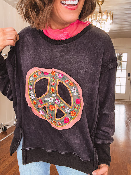 Washed charcoal pullover with exposed seams, a coral and floral peace patch on the front and split front hem.