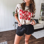 100% Cotton  tee with bold red "Smoke Show" graphic against an artistic tan and brown paint splatter backdrop.