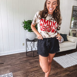 100% Cotton  tee with bold red "Smoke Show" graphic against an artistic tan and brown paint splatter backdrop.