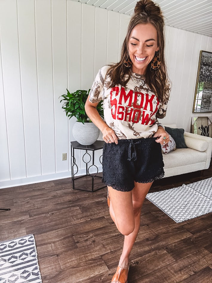 100% Cotton  tee with bold red "Smoke Show" graphic against an artistic tan and brown paint splatter backdrop.