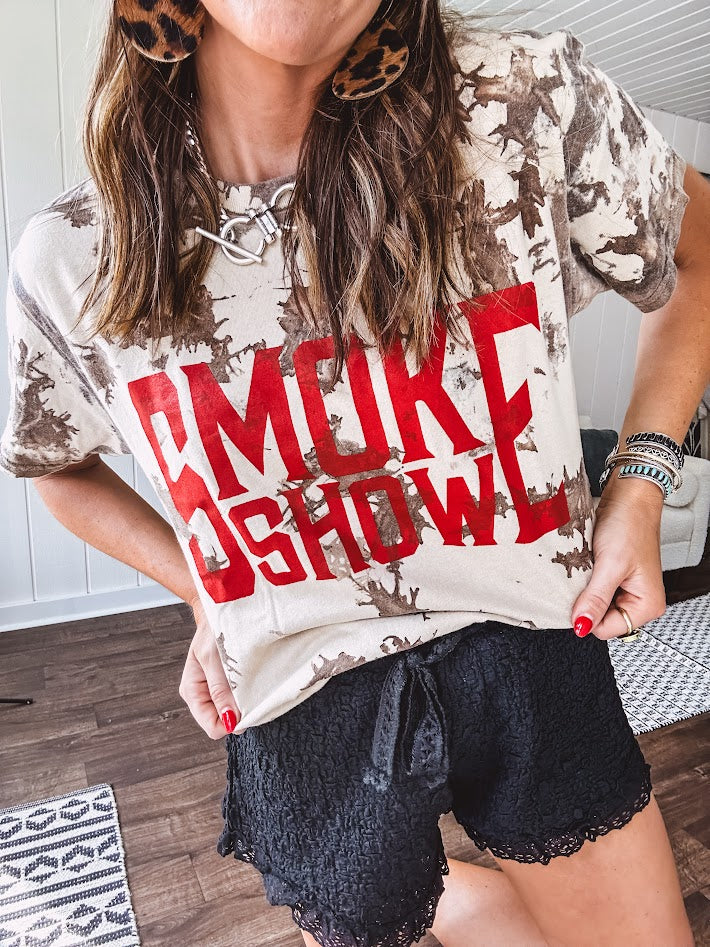 100% Cotton  tee with bold red "Smoke Show" graphic against an artistic tan and brown paint splatter backdrop.