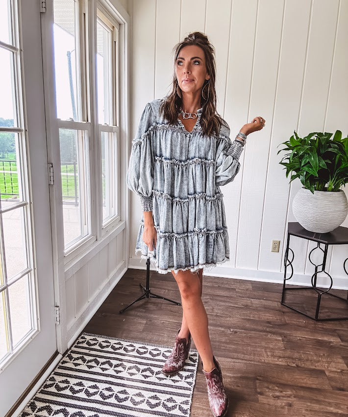 Soft, lightweight Tencel denim mini dress in a retro acid wash design with a V neck and mock collar and tiered design with long sleeves and elastic cuffs each tier and the mock neck feature raw seams and it has pockets.