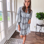 Soft, lightweight Tencel denim mini dress in a retro acid wash design with a V neck and mock collar and tiered design with long sleeves and elastic cuffs each tier and the mock neck feature raw seams and it has pockets.