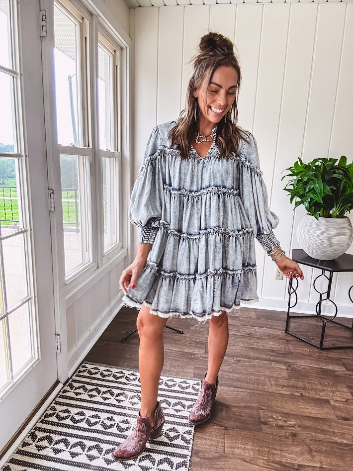 Soft, lightweight Tencel denim mini dress in a retro acid wash design with a V neck and mock collar and tiered design with long sleeves and elastic cuffs each tier and the mock neck feature raw seams and it has pockets.
