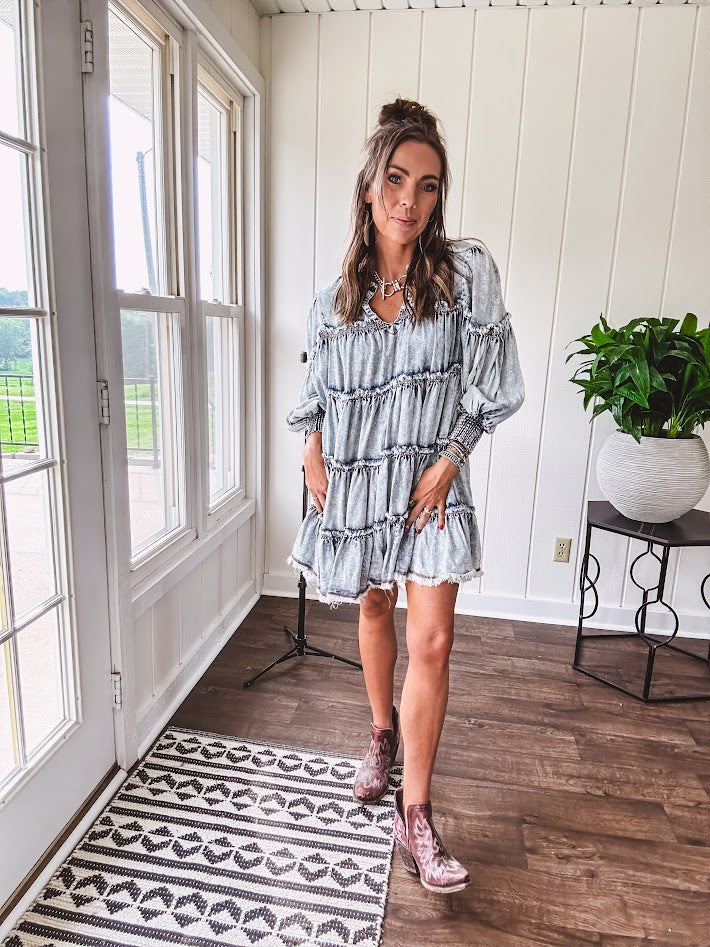 Soft, lightweight Tencel denim mini dress in a retro acid wash design with a V neck and mock collar and tiered design with long sleeves and elastic cuffs each tier and the mock neck feature raw seams and it has pockets.