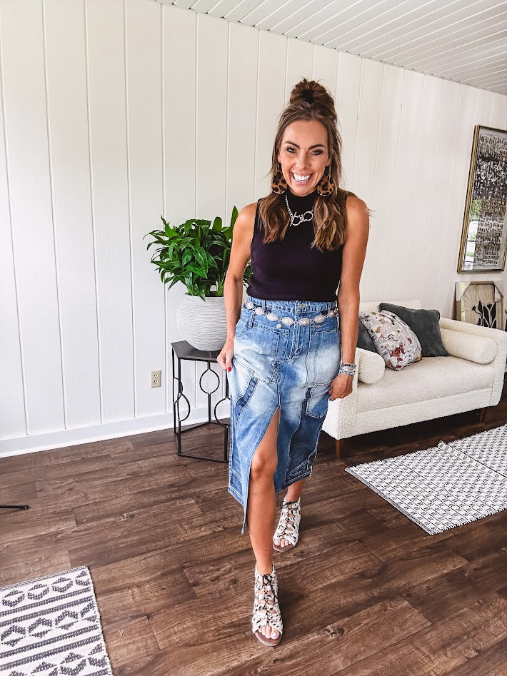 Medium wash midi skirt featuring light and dark wash details throughout with a button and zipper closure and elastic back waist, high front split, side pockets and an upside down design on the bottom. 