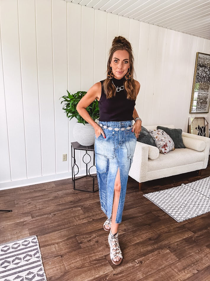 Medium wash midi skirt featuring light and dark wash details throughout with a button and zipper closure and elastic back waist, high front split, side pockets and an upside down design on the bottom. 