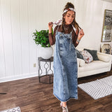 Medium wash denim dress with spaghetti straps and silver metal adjusters, a unique button and zipper front resembling the top of a pair of jeans, back pockets, side pockets, a back slit and raw hem.