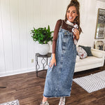 Medium wash denim dress with spaghetti straps and silver metal adjusters, a unique button and zipper front resembling the top of a pair of jeans, back pockets, side pockets, a back slit and raw hem.