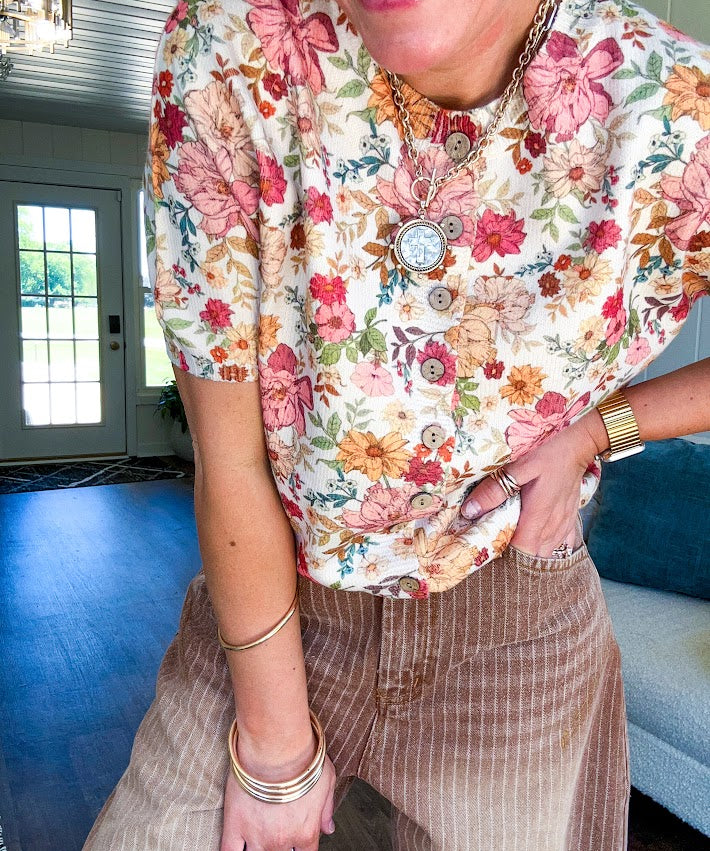 Soft, short sleeved button front sweater with Earth toned florals throughout, faux wooden buttons and round neck.