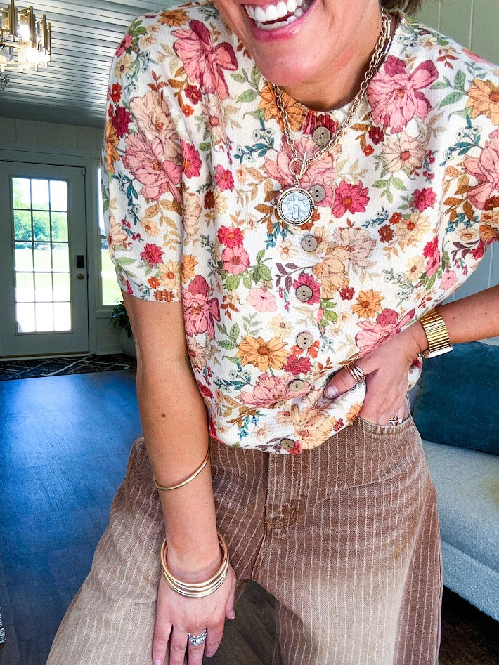 Soft, short sleeved button front sweater with Earth toned florals throughout, faux wooden buttons and round neck.