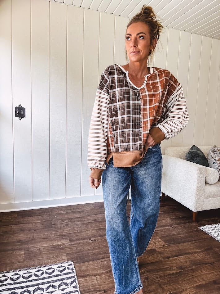 Plaid pullover pairs earth-tone mocha, cream, and rust with playful contrasting stripes on the sleeves with a split neck and relaxed fit.