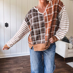 Plaid pullover pairs earth-tone mocha, cream, and rust with playful contrasting stripes on the sleeves with a split neck and relaxed fit.