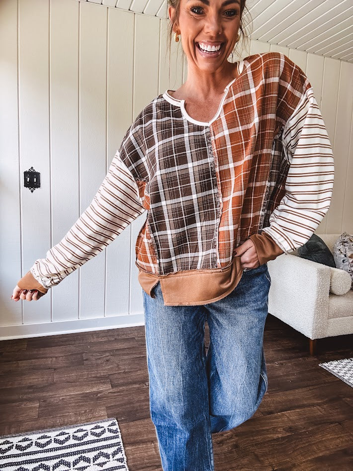 Plaid pullover pairs earth-tone mocha, cream, and rust with playful contrasting stripes on the sleeves with a split neck and relaxed fit.