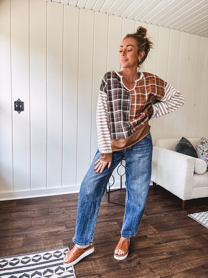 Plaid pullover pairs earth-tone mocha, cream, and rust with playful contrasting stripes on the sleeves with a split neck and relaxed fit.