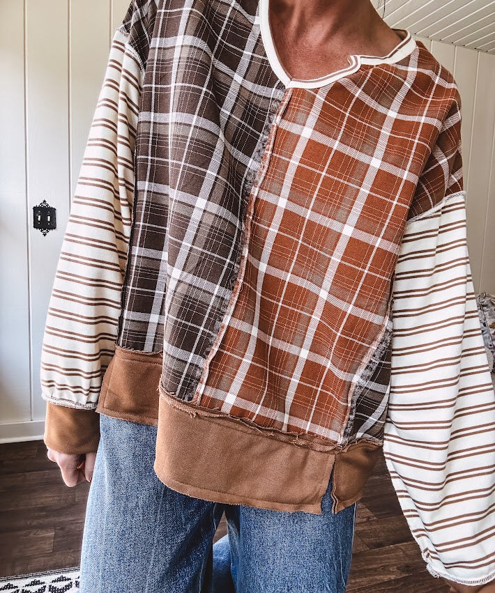 Plaid pullover pairs earth-tone mocha, cream, and rust with playful contrasting stripes on the sleeves with a split neck and relaxed fit.