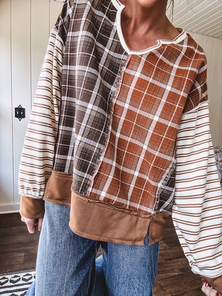 Plaid pullover pairs earth-tone mocha, cream, and rust with playful contrasting stripes on the sleeves with a split neck and relaxed fit.